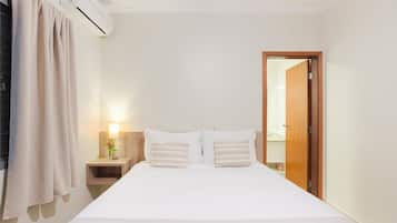 Un dormitorio con una cama, mesitas de noche, una lámpara y una puerta.