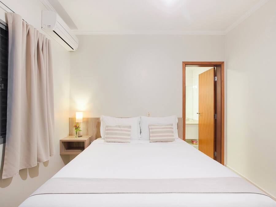 Un dormitorio con una cama, mesitas de noche, una lámpara y una puerta.