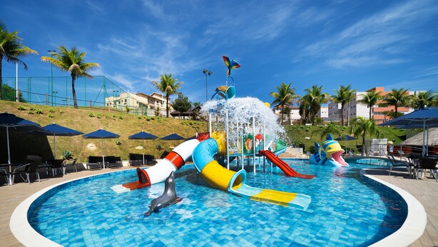 Una piscina con tobogán de agua, sillas de descanso y sombrillas.