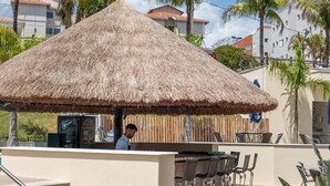 Una estructura con techo de paja, que incluye una barra y mesas al aire libre.