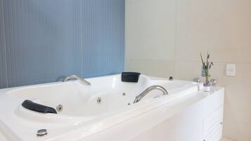 A modern bathroom with a large white bathtub, a black bath mat, and a small potted plant on the vanity.