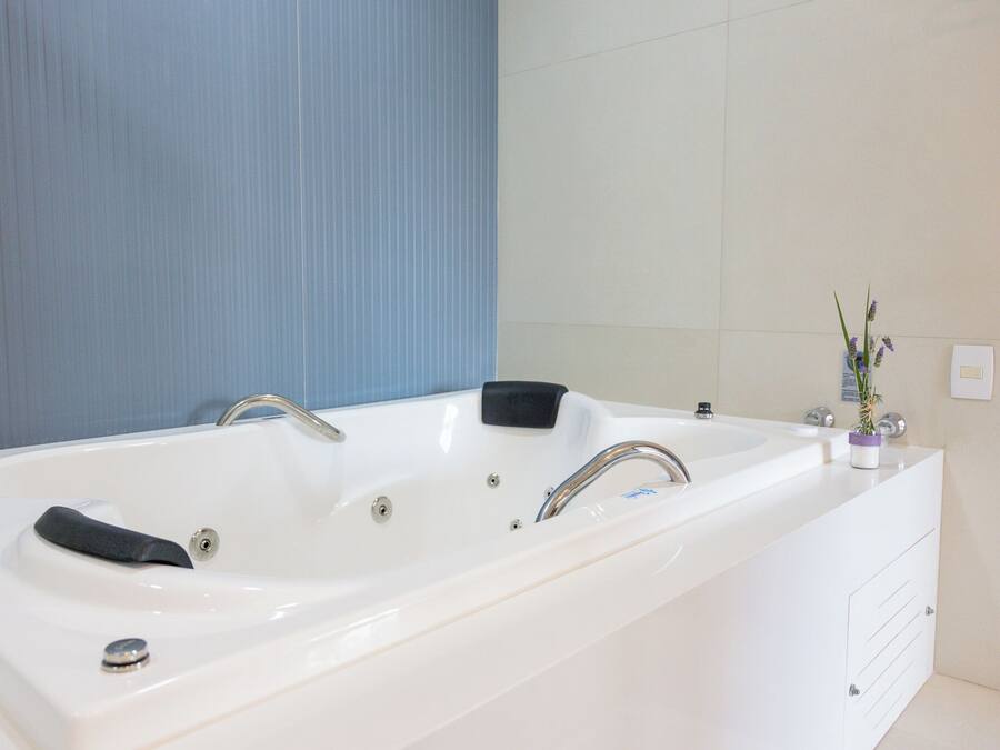 A modern bathroom with a large white bathtub, a black bath mat, and a small potted plant on the vanity.