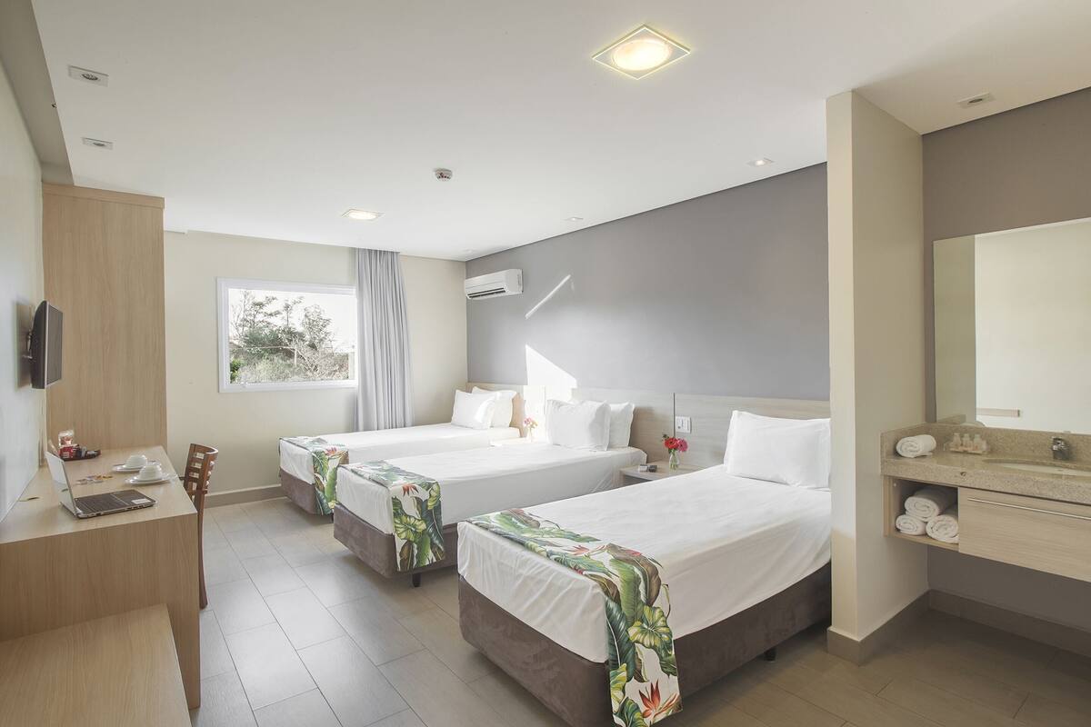 Une chambre d’hôtel avec deux lits, un bureau avec un ordinateur portable, une télévision et une salle de bain équipée d’un miroir et d’un porte-serviettes.