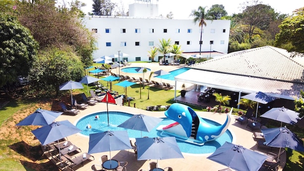 Een hotel met meerdere zwembaden, ligbedden, parasols en een groot gebouw op de achtergrond.