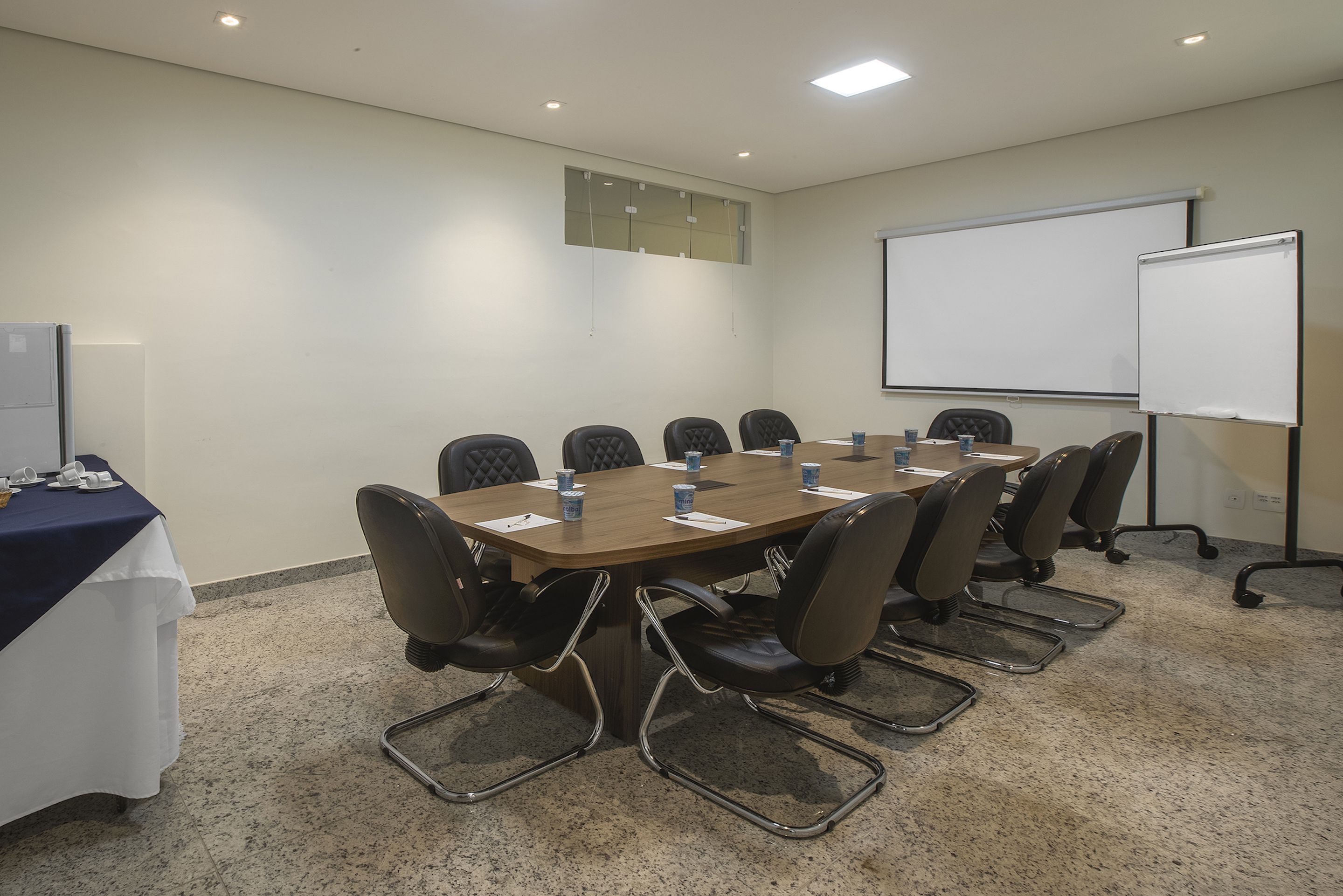 A conference room with a large table, eight chairs, a whiteboard, and a projector screen.