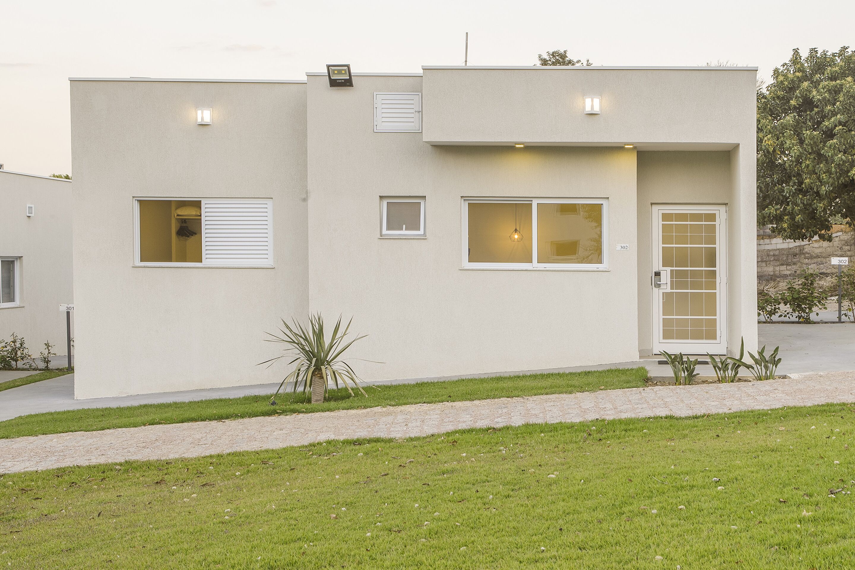 Un edificio moderno de dos pisos con techo plano, un pequeño porche y una puerta con panel de vidrio.