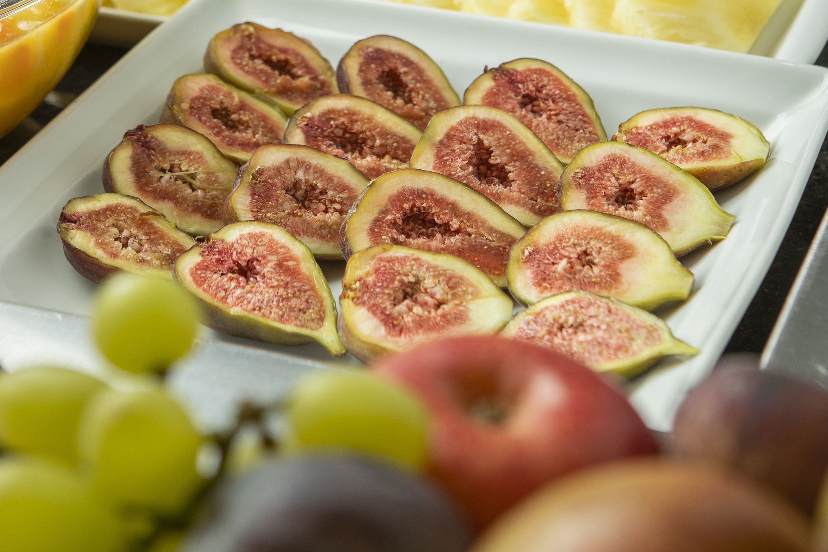 Un plato blanco con higos y uvas cortados.