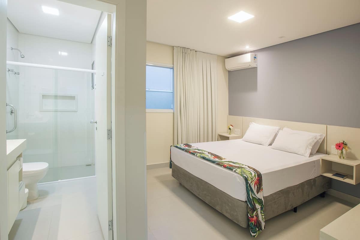 Une chambre d’hôtel équipée d’une douche, de toilettes, d’un lit, d’une table de chevet et d’une fenêtre.