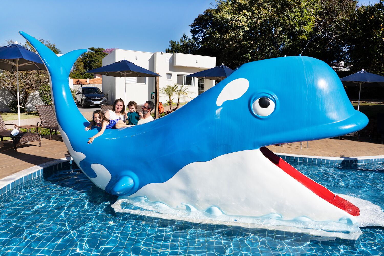 Une piscine avec un grand toboggan en forme de baleine, des chaises longues et des parasols.