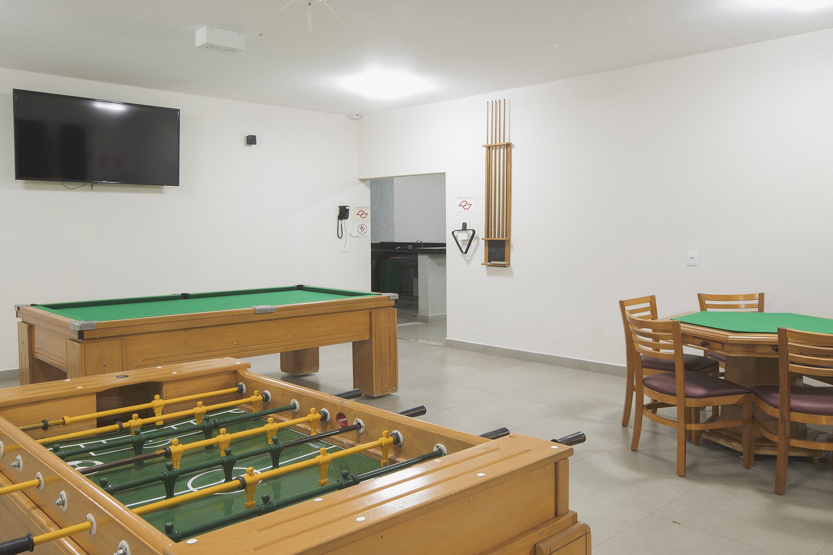 A billiards room with a pool table, foosball table, and a television mounted on the wall.