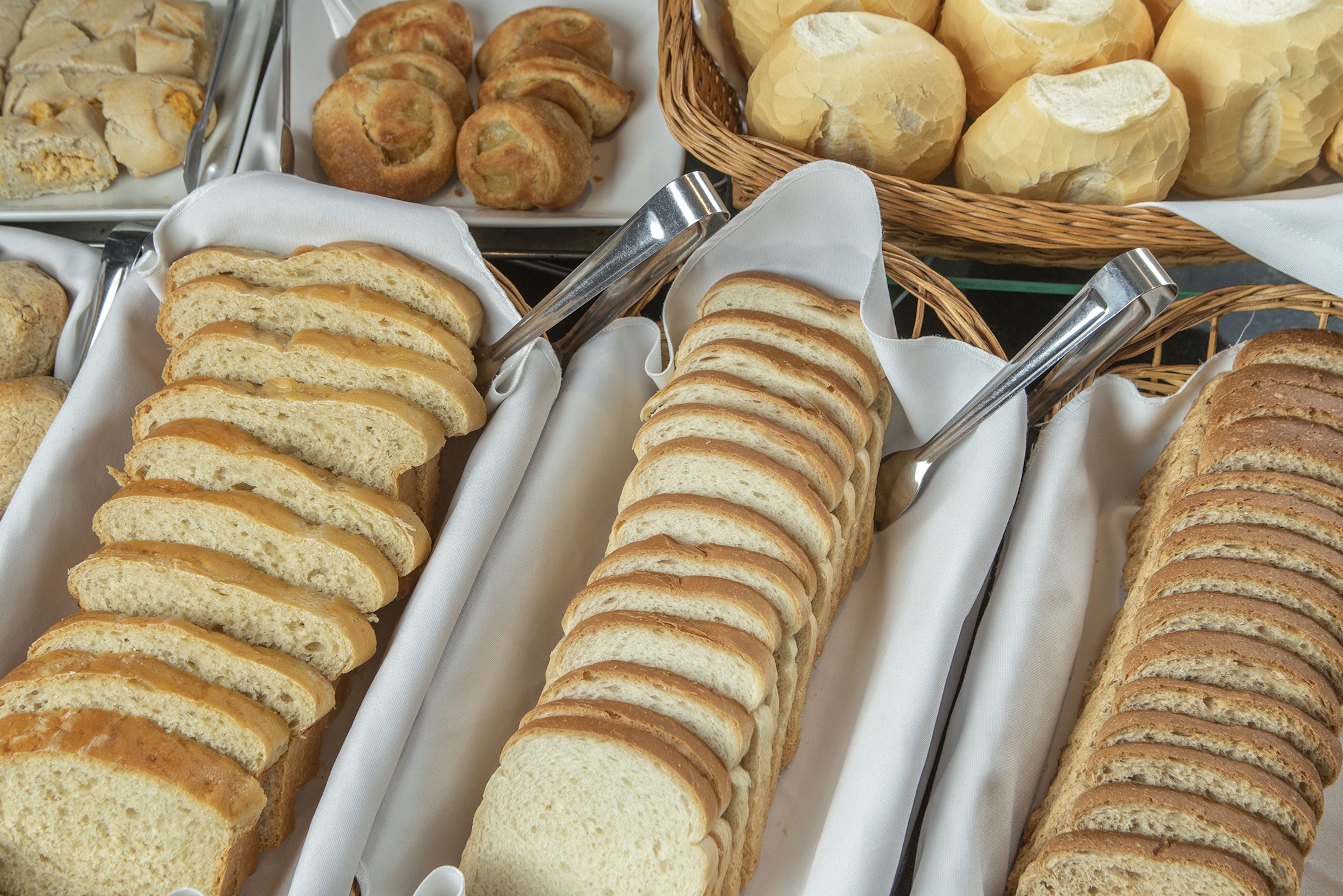 A variety of sliced bread displayed in trays, with a basket of whole loaves in the background.