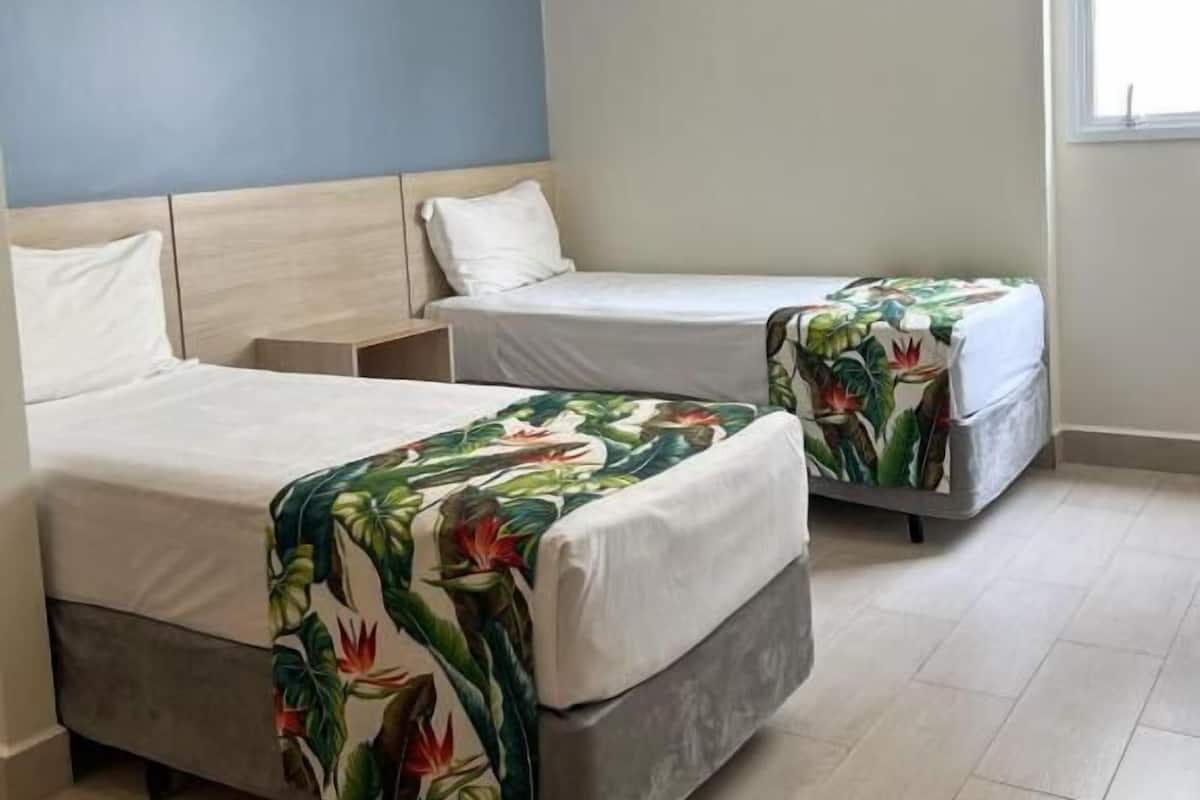Une chambre d’hôtel avec deux lits simples, une table de chevet, une fenêtre et un mur bleu.