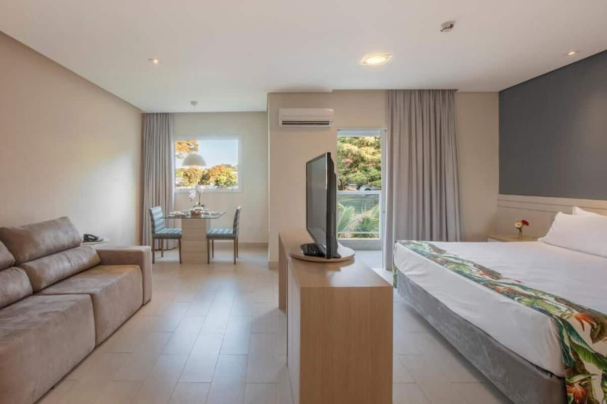 Une chambre d’hôtel avec un lit, un canapé, un téléviseur posé sur un meuble, une petite table et une fenêtre avec des rideaux.