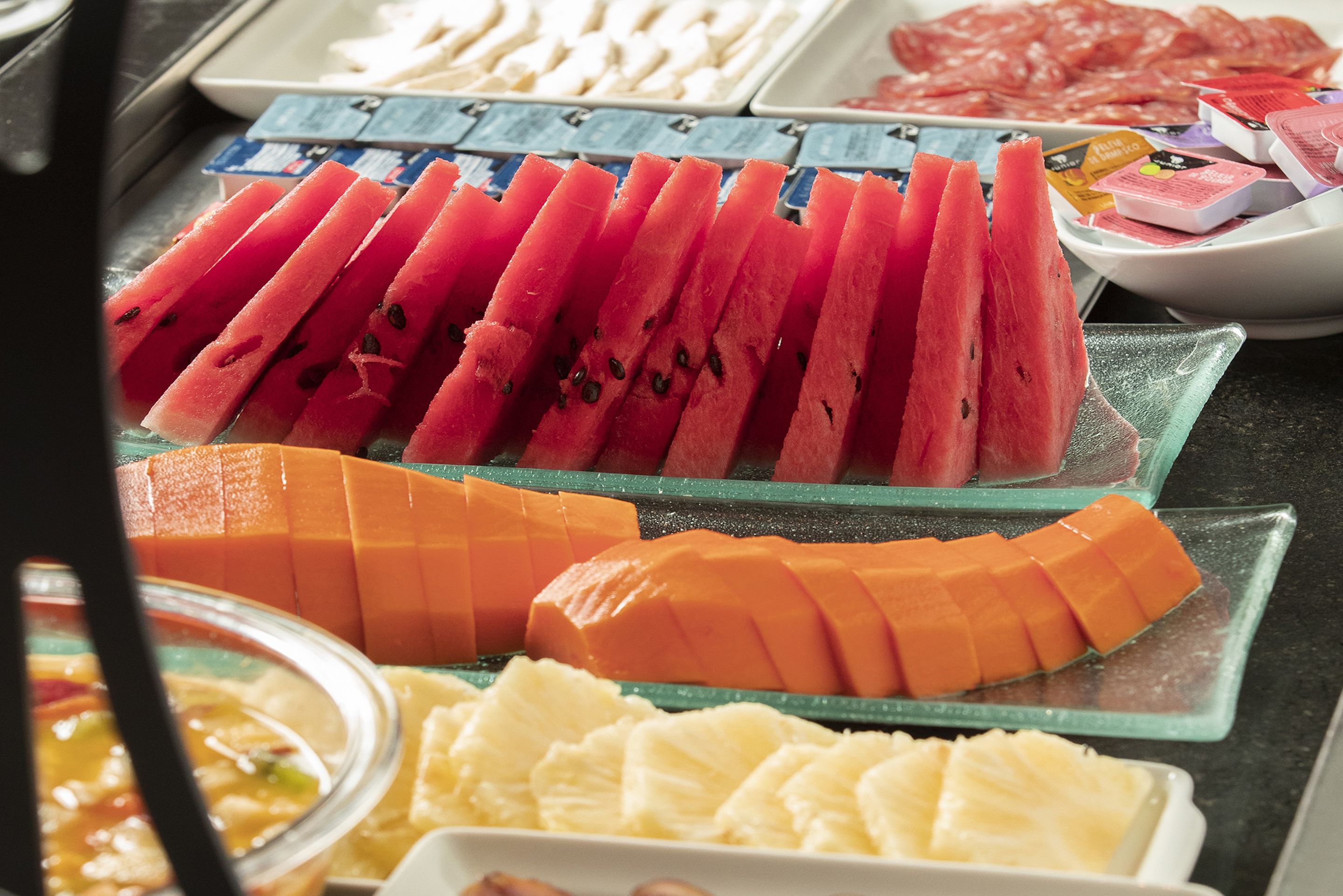 A selection of fresh fruits including watermelon, mango, and pineapple arranged on glass trays.