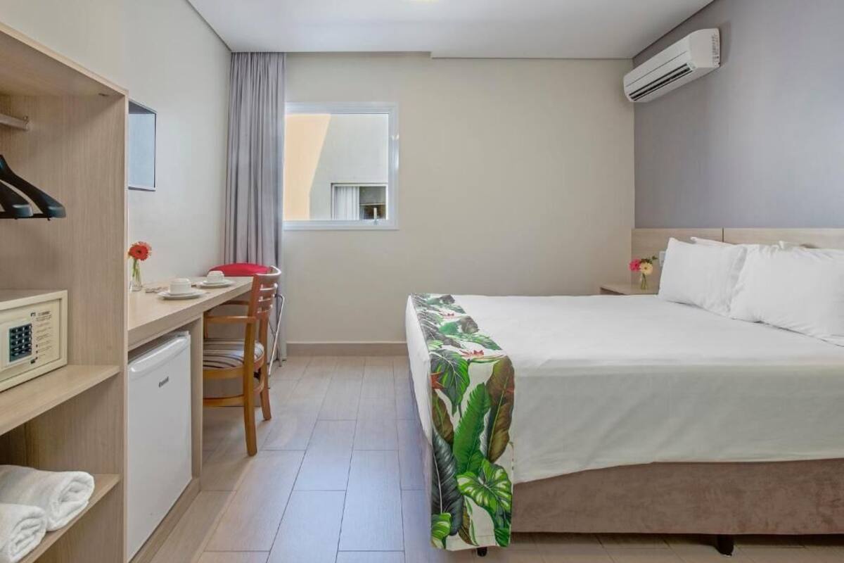 Une chambre d’hôtel équipée d’un lit, d’un bureau, d’une chaise, d’un petit réfrigérateur et d’une fenêtre avec des rideaux.