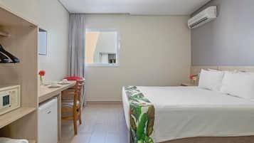 Quarto de hotel com cama, escrivaninha, cadeira, mini-frigorífico e janela com cortinas.