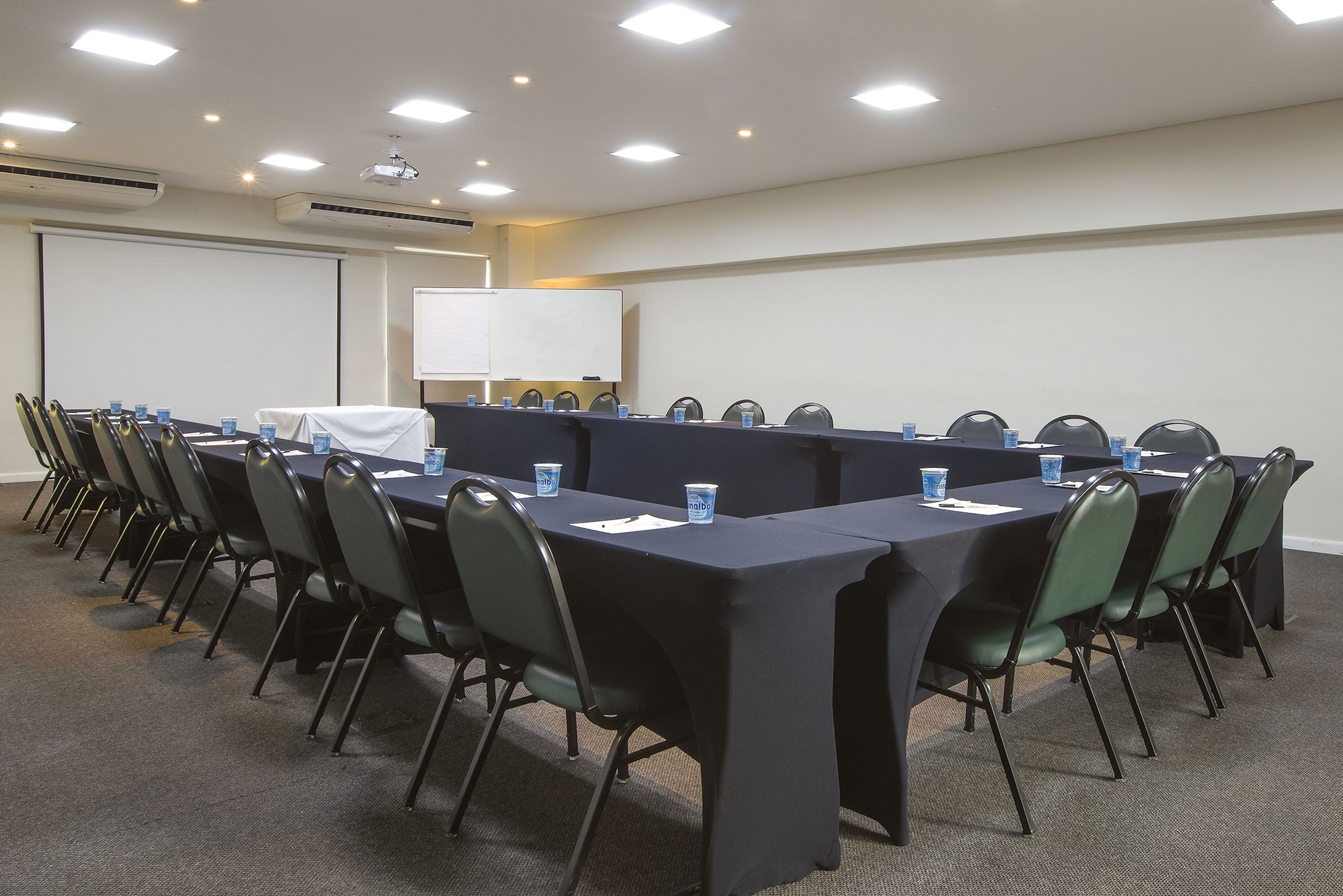 Una sala de conferencias con una larga mesa, sillas, una pantalla de proyector y una pizarra.