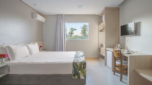 Een moderne hotelkamer met een groot bed, een bureau met stoel, een televisie en een raam met uitzicht op bomen.