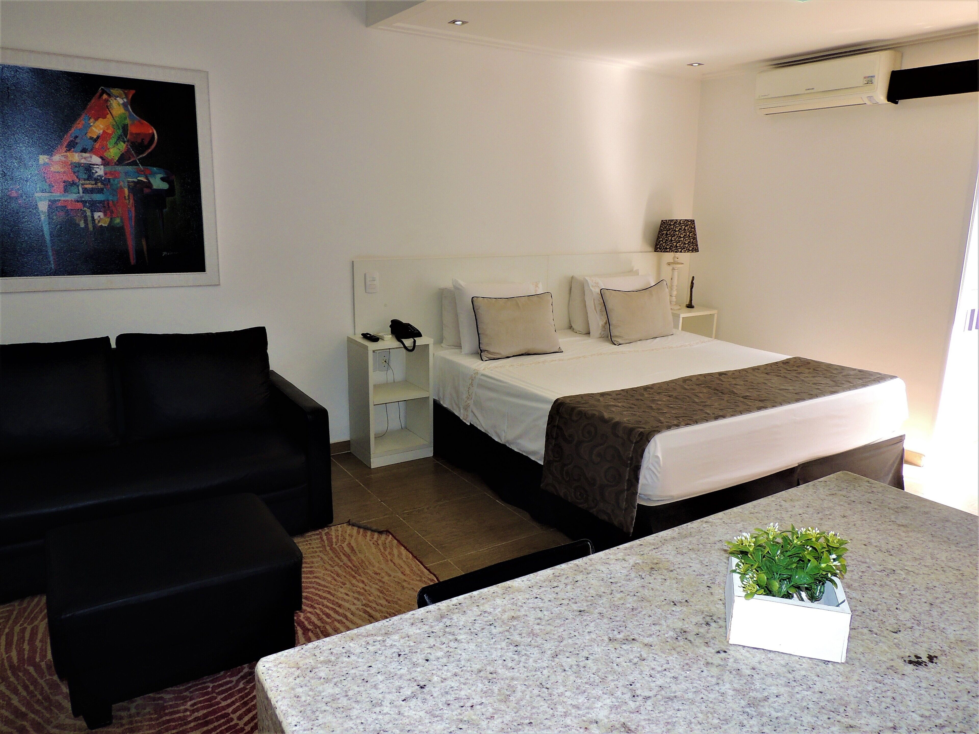 A hotel room with a bed, a desk, a chair, a nightstand, a lamp, and a painting on the wall.