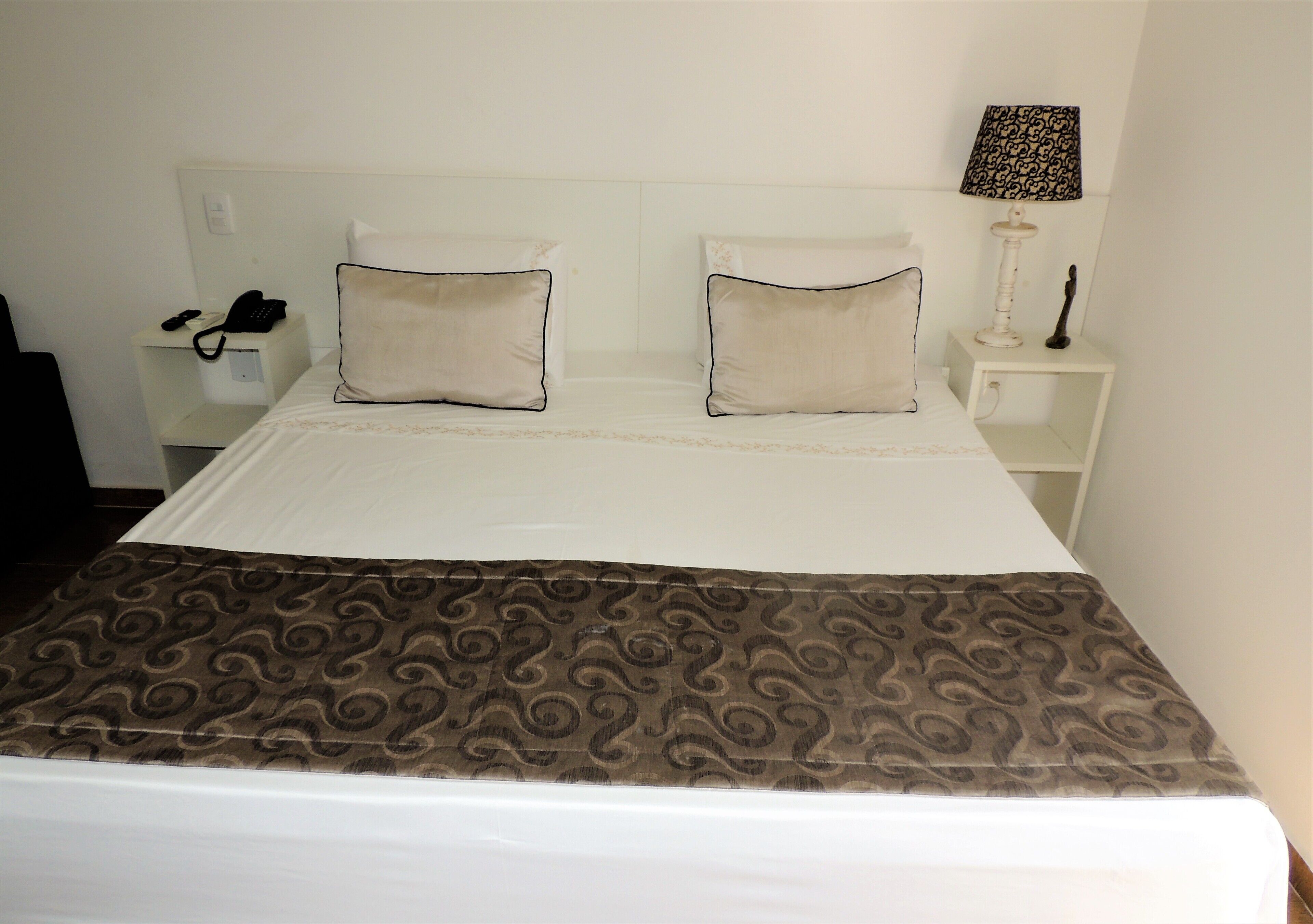 A neatly made bed with a patterned bedspread, two pillows, a bedside lamp, and a telephone on a bedside table.