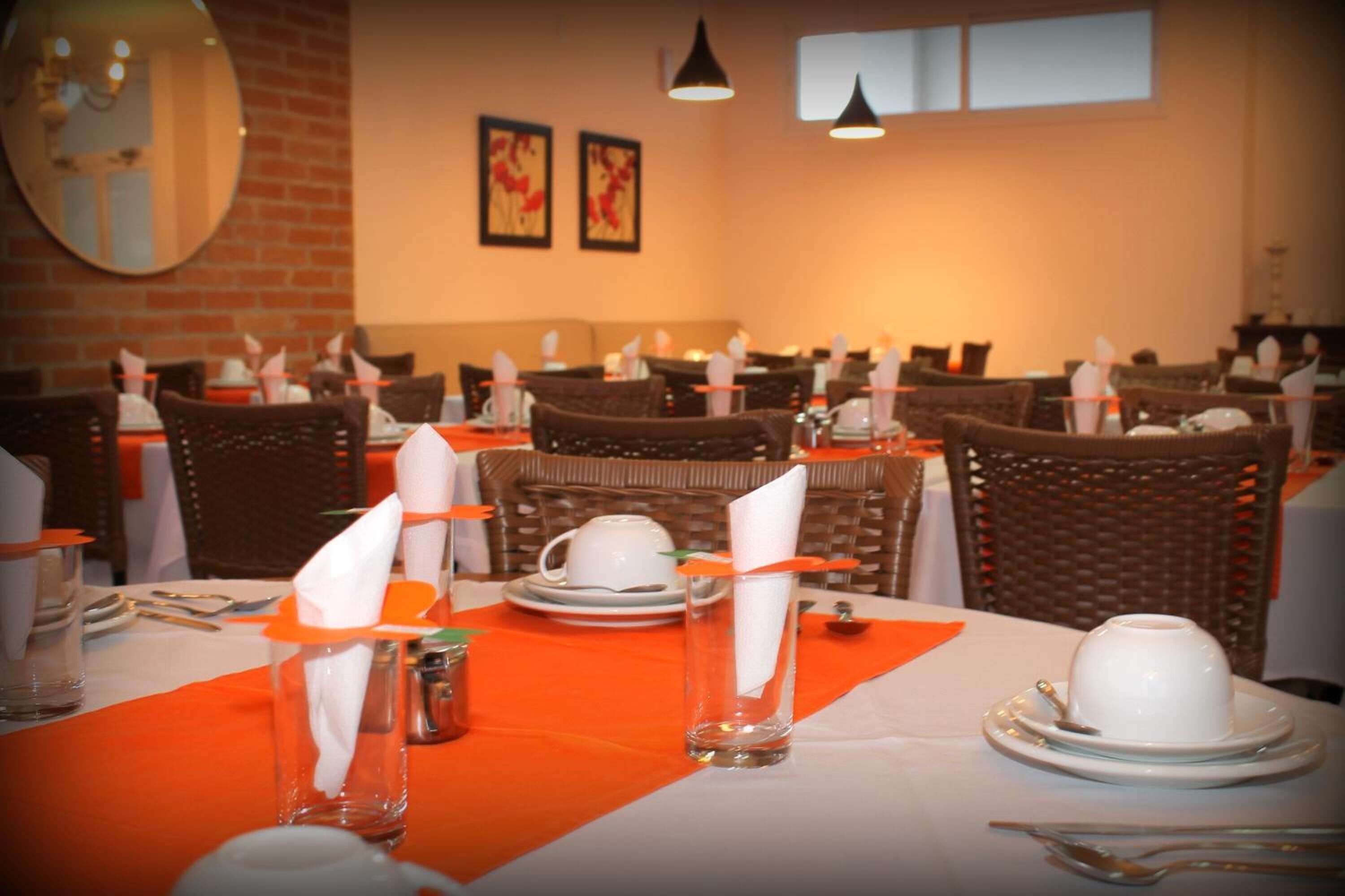 A restaurant with multiple tables set with white tablecloths, orange placemats, and white napkins.