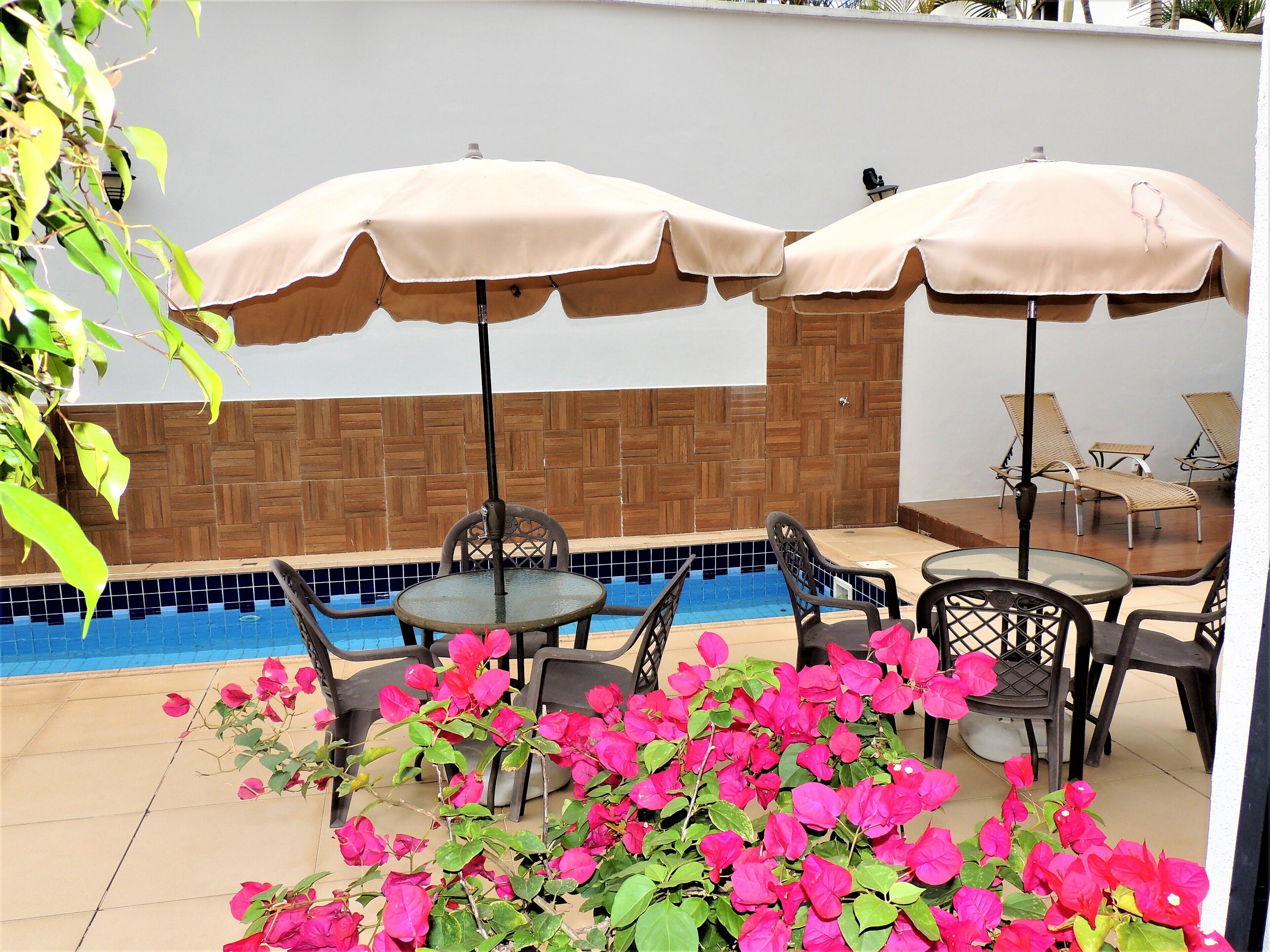 A poolside area with two tables and chairs, two umbrellas, and a tiled wall.