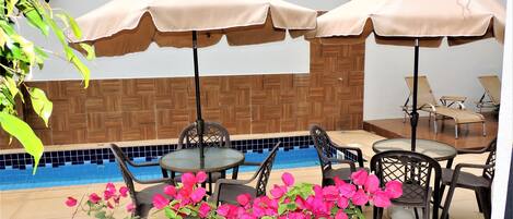 A poolside area with two tables and chairs, two umbrellas, and a tiled wall.