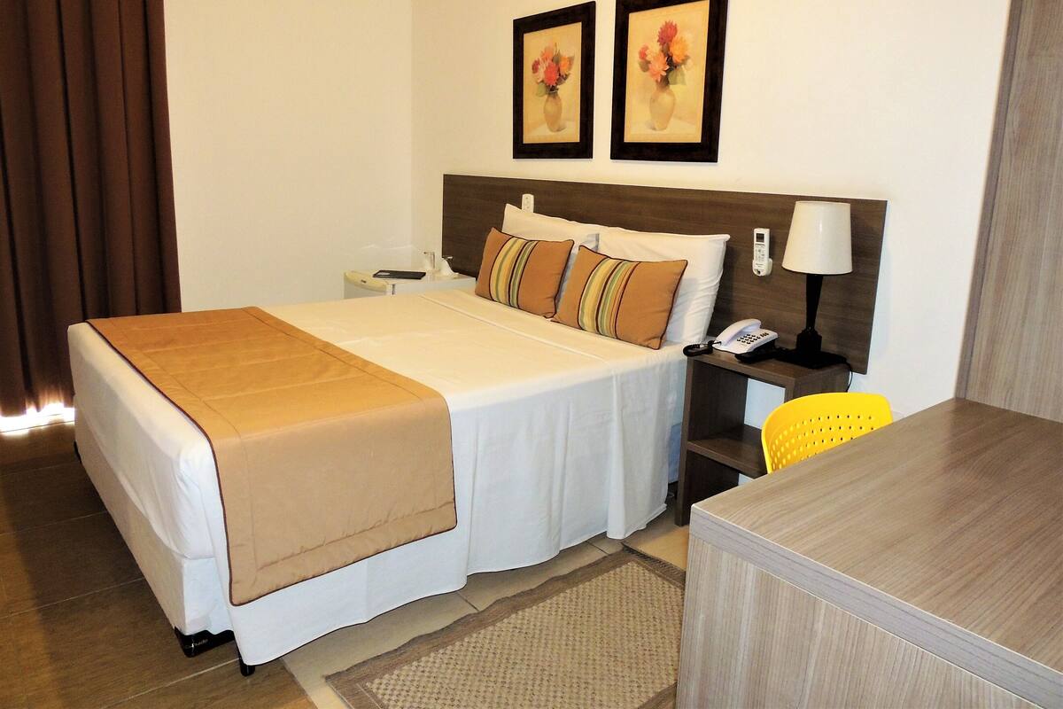A hotel room with a bed, bedside table, lamp, and a chair.
