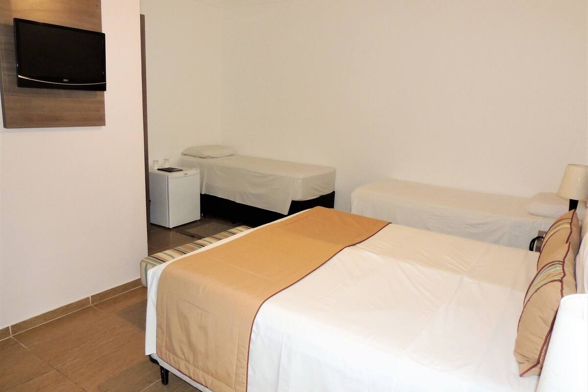 A hotel room with a large bed, a smaller bed, a TV mounted on the wall, a bedside table, and a lamp.
