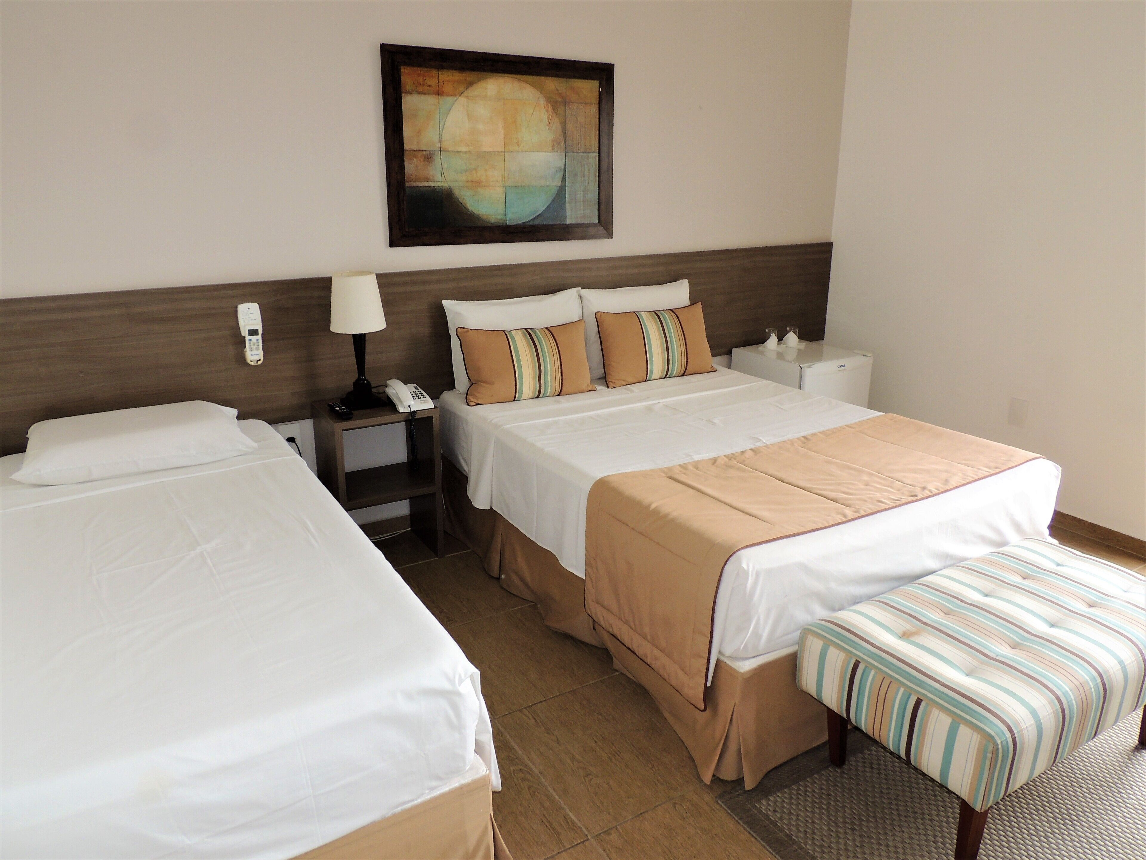 A hotel room with two beds, a bedside table with a lamp, a telephone, and a painting on the wall.
