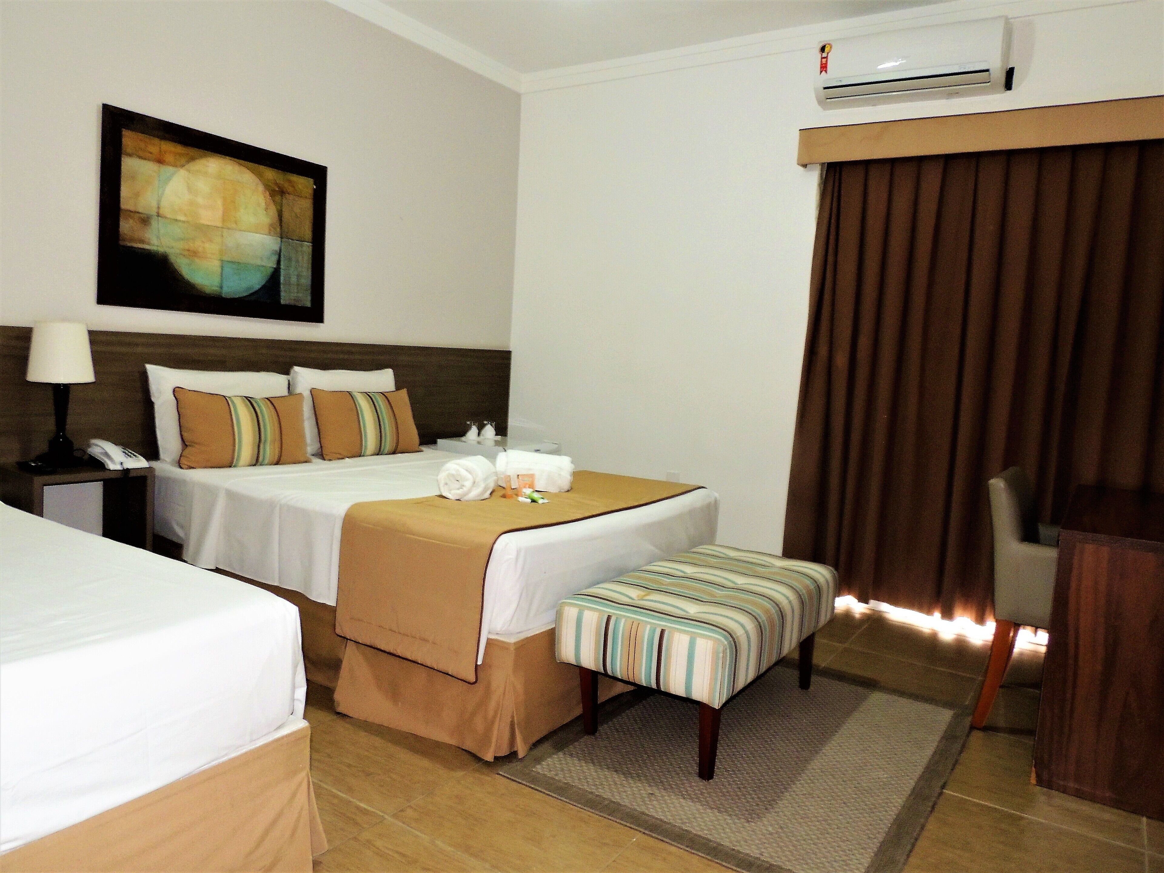 A hotel room with two beds, a desk, a chair, and an air conditioning unit.