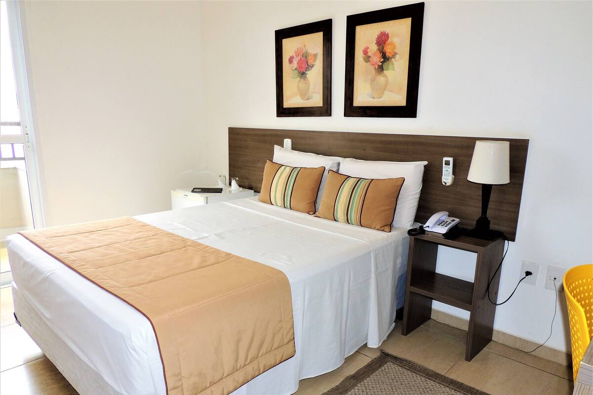 A neatly made bed with a beige blanket, a bedside table with a lamp, and two framed floral paintings on the wall.