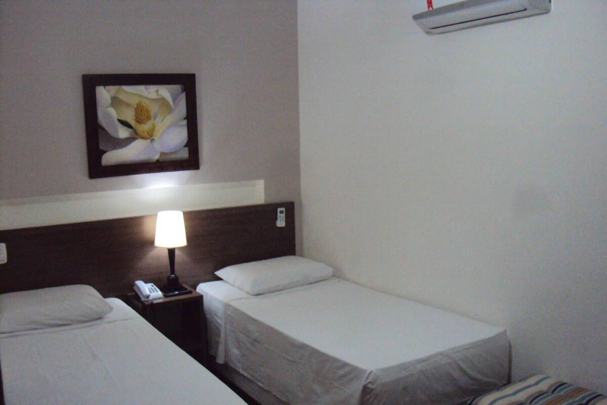 A hotel room with two single beds, a nightstand with a lamp, a phone, and a framed picture on the wall.