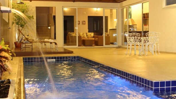 Una piscina con fuente de agua, un patio cubierto con mobiliario exterior y vista a una sala de estar.