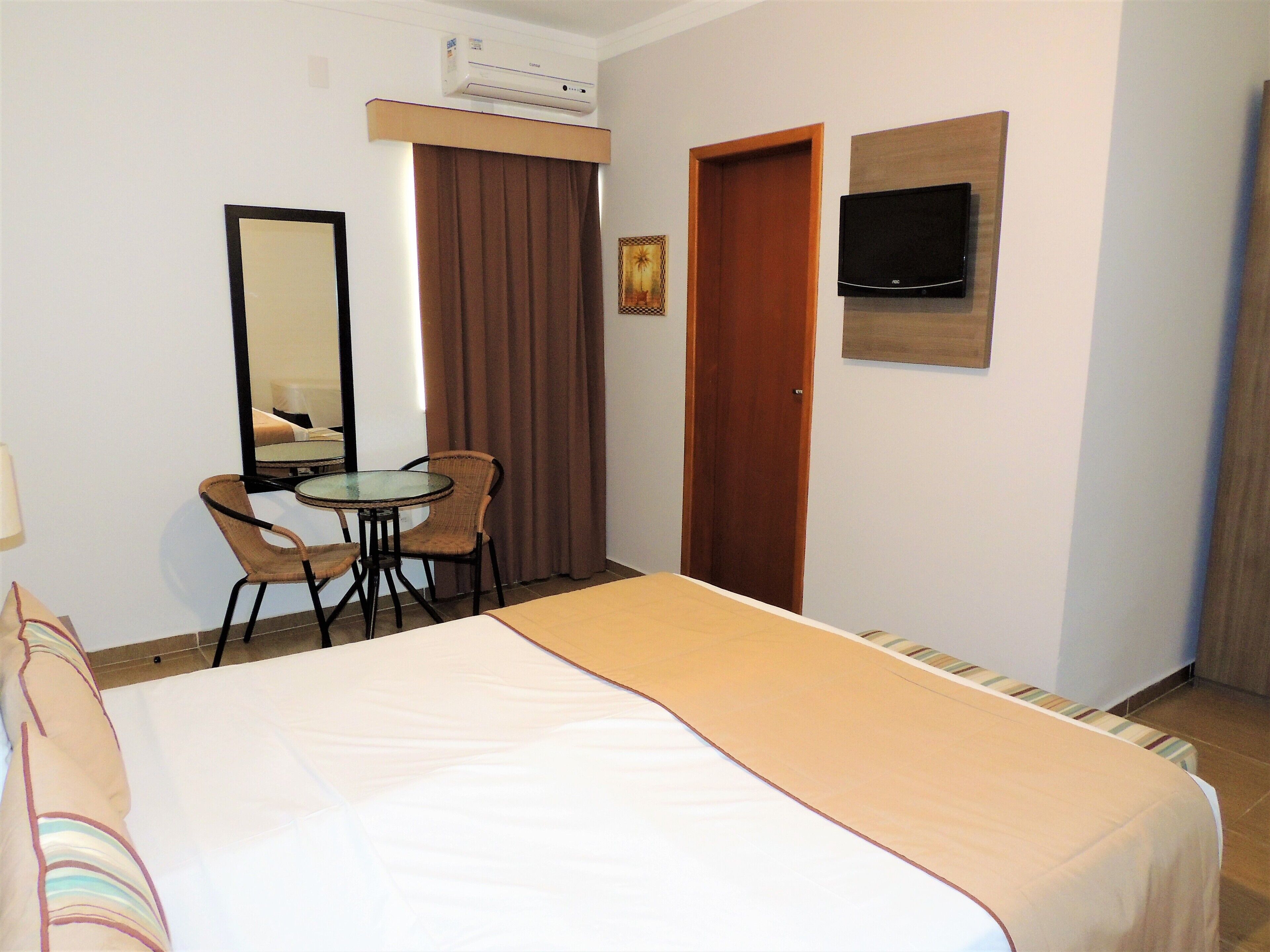 Una habitación de hotel con una cama, un escritorio y dos sillas, un televisor montado en la pared y una puerta.