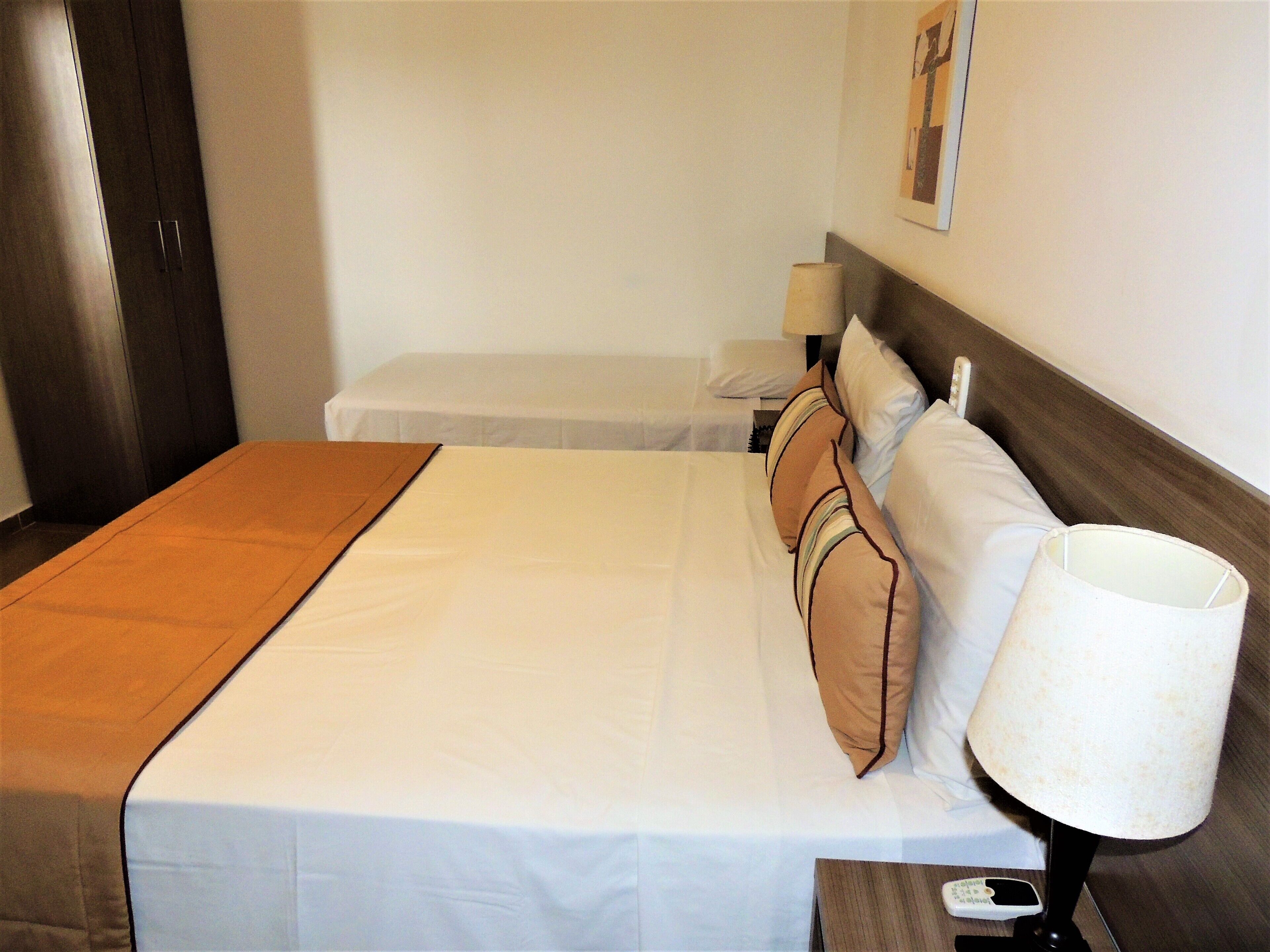 Una cama bien hecha con cubrecama blanco y almohadas marrones, una mesita de noche de madera con una lámpara y un cabecero de madera.
