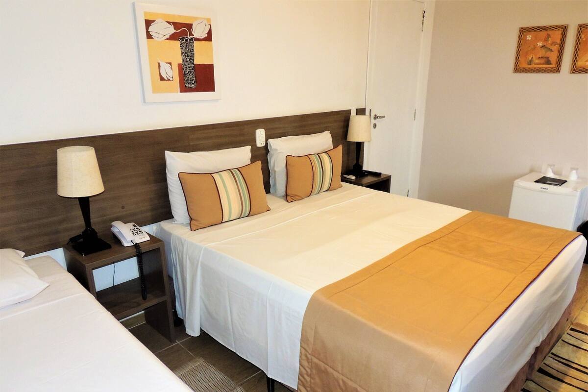 A hotel room with a large bed, two bedside tables, a nightstand, a lamp, a telephone, and a wall-mounted artwork.