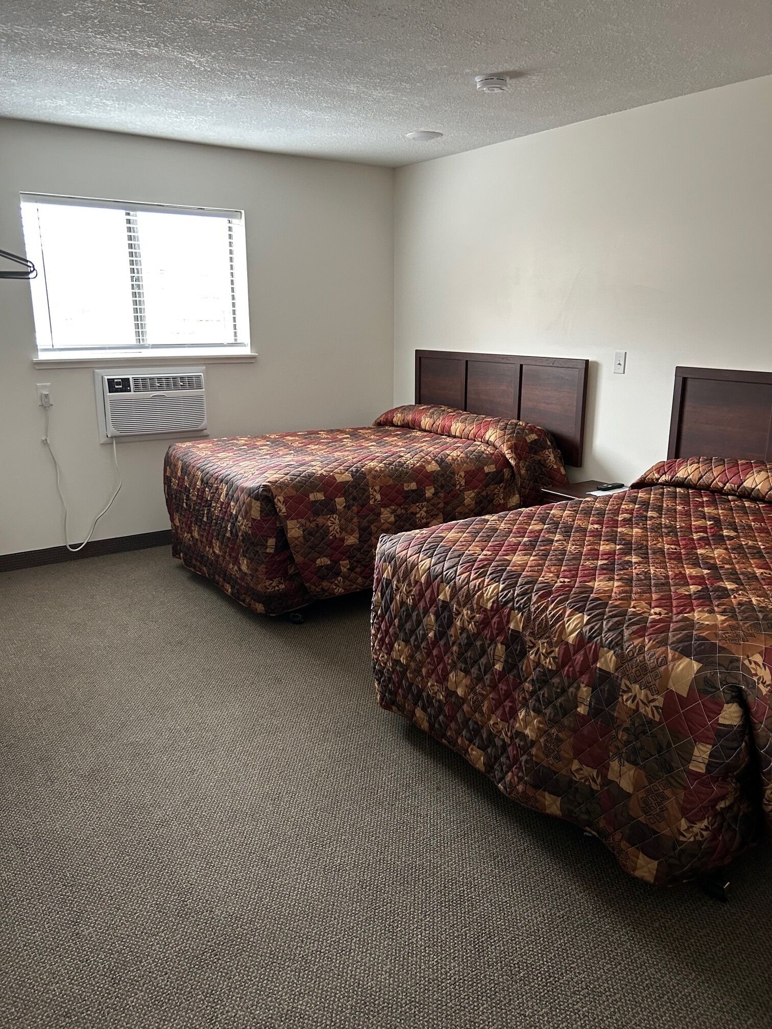 Habitación de hotel con dos camas, una ventana, equipo de aire acondicionado y piso alfombrado.