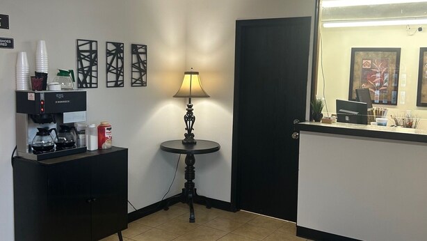 Un hall d’hôtel comprenant un comptoir d’accueil, une machine à café, une petite table avec une lampe et des œuvres d’art encadrées accrochées aux murs.