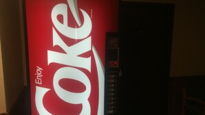 Un distributeur automatique arborant un logo Coca-Cola bien visible et le mot «Profitez» dessus.