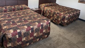 Une chambre d’hôtel avec deux lits, chacun recouvert d’une courtepointe à motifs, une table de chevet et une lampe fixée au mur.