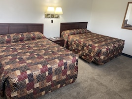 Habitación de hotel con dos camas, cada una con una colcha estampada, una mesita de noche y una lámpara de pared.