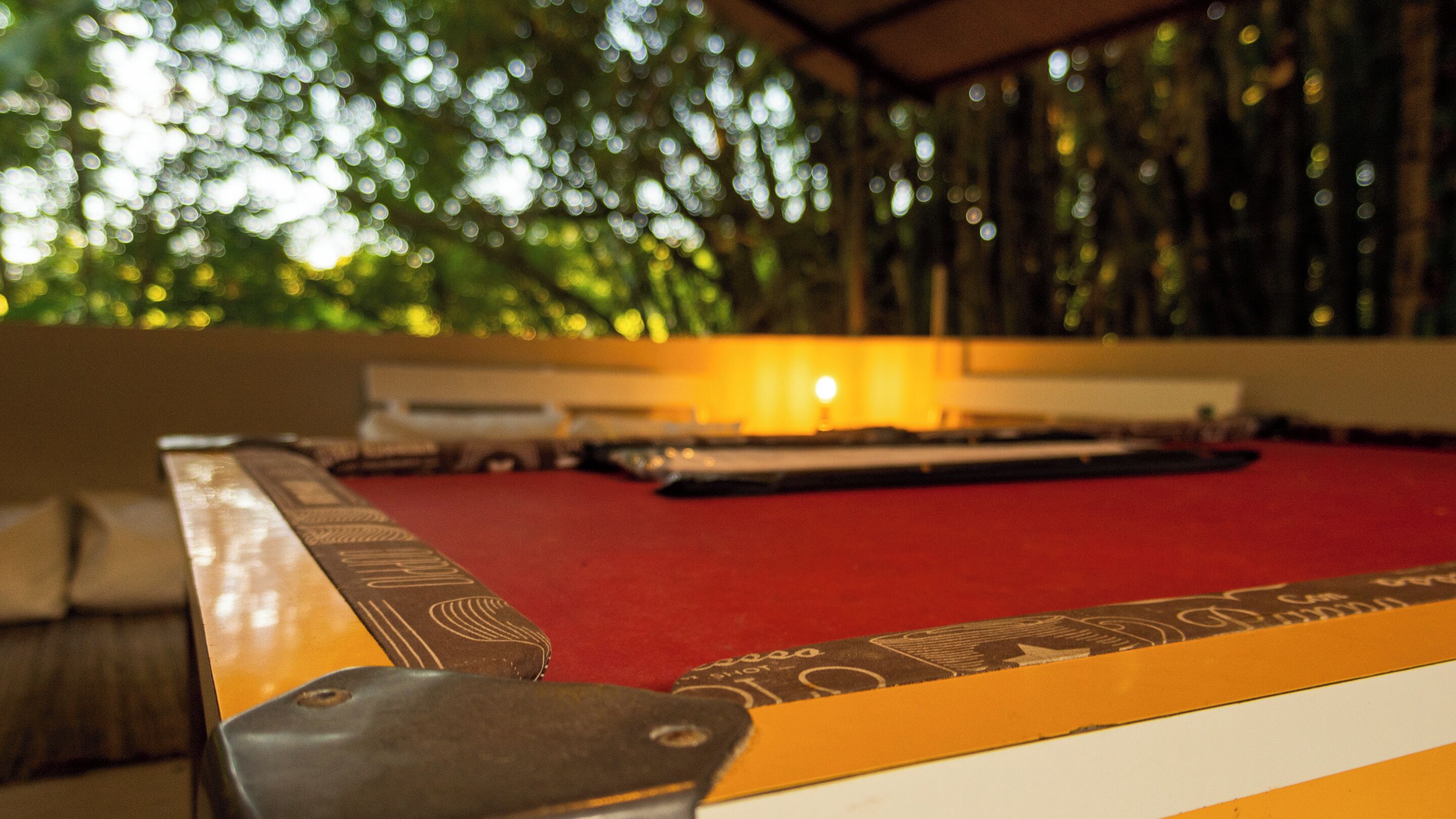 A pool table with a red felt surface, surrounded by a wooden frame with a patterned design.