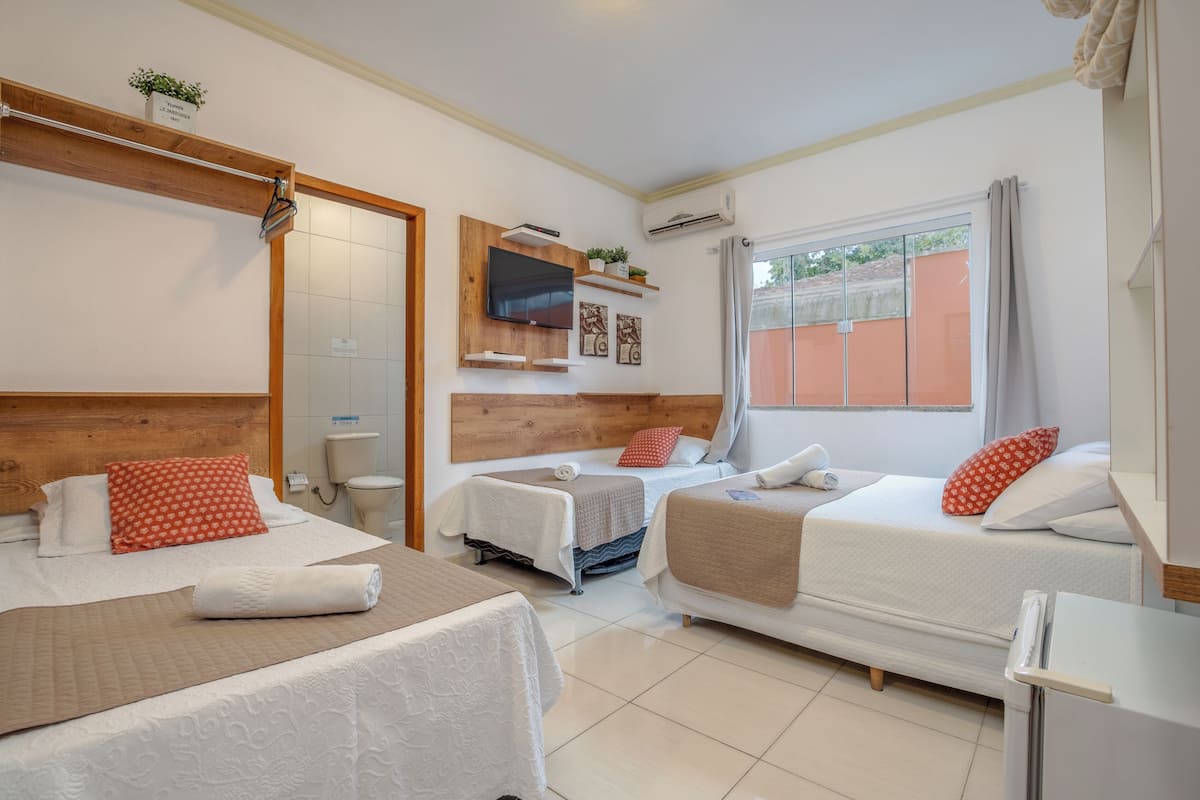 A hotel room with two beds, a TV, a window with curtains, and a small table.