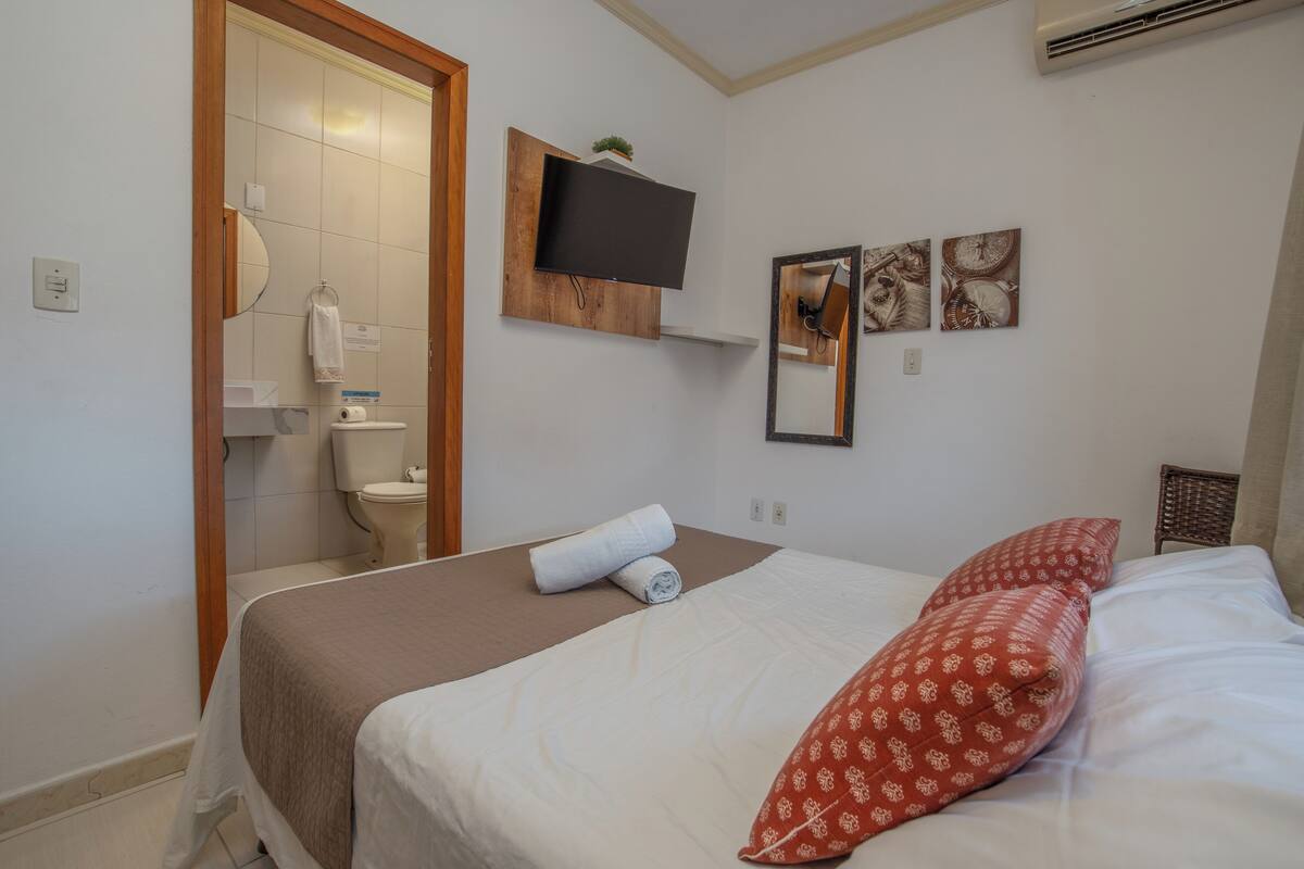 A hotel room with a bed, a mounted TV, a mirror, and artwork on the wall.