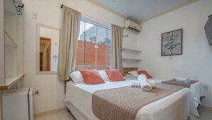 Ein Hotelzimmer mit einem großen Bett, einem kleineren Bett, einem Fenster mit Vorhängen, einer wandmontierten Klimaanlage und einem kleinen Kühlschrank.