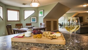 A dining area with a marble table, a wooden board with cheese, grapes, and crackers, and a glass of white wine. - Wheat City Retreat (Brandon)