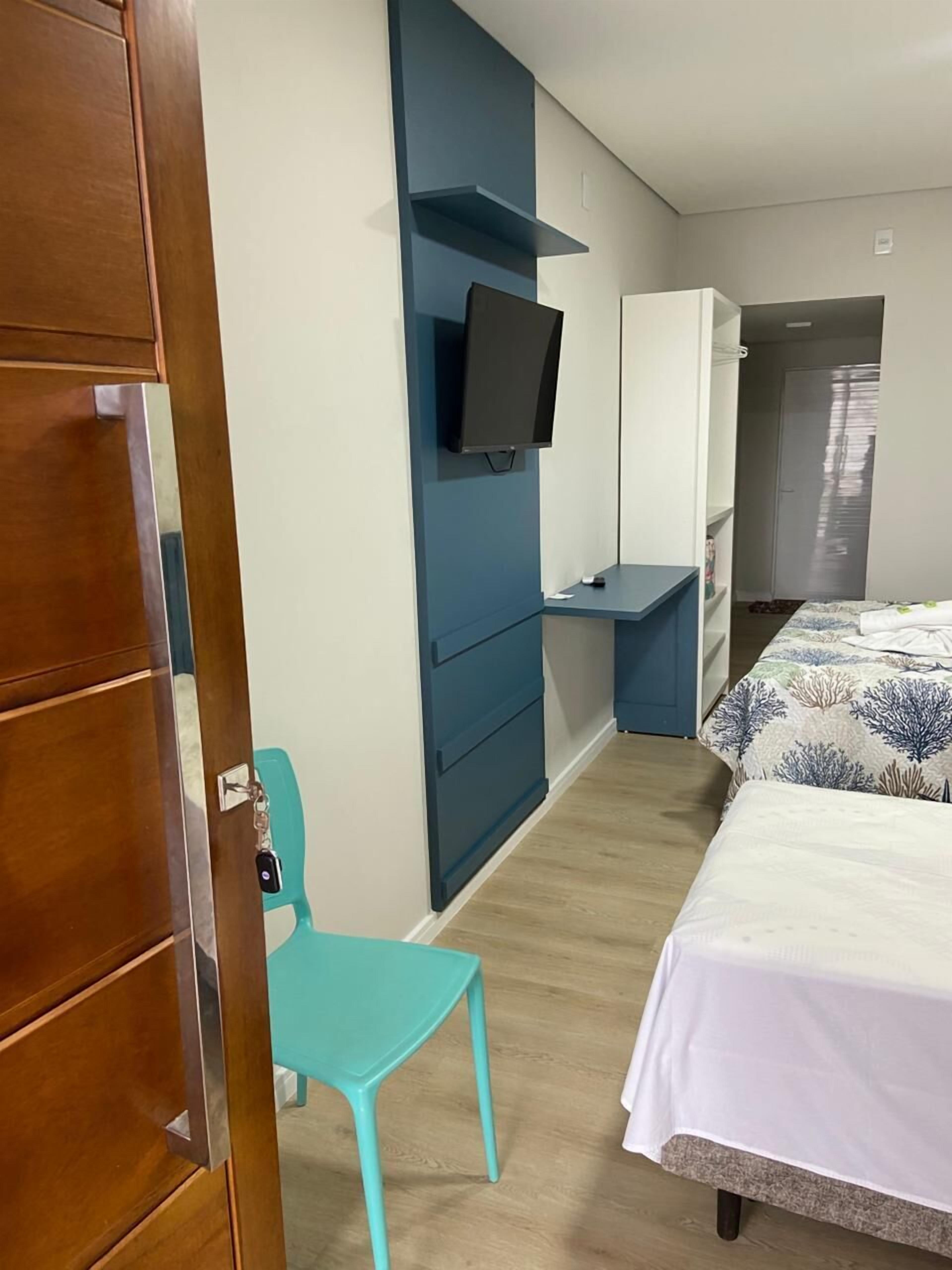 Une chambre d’hôtel comprenant un lit, un bureau avec une chaise, un téléviseur fixé au mur et une armoire.