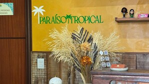 A reception desk with a sign reading "Paraíso Tropical," a vase with dried flowers, a coffee maker, and a tray with snacks. - Pousada Paraíso Tropical (Penha)