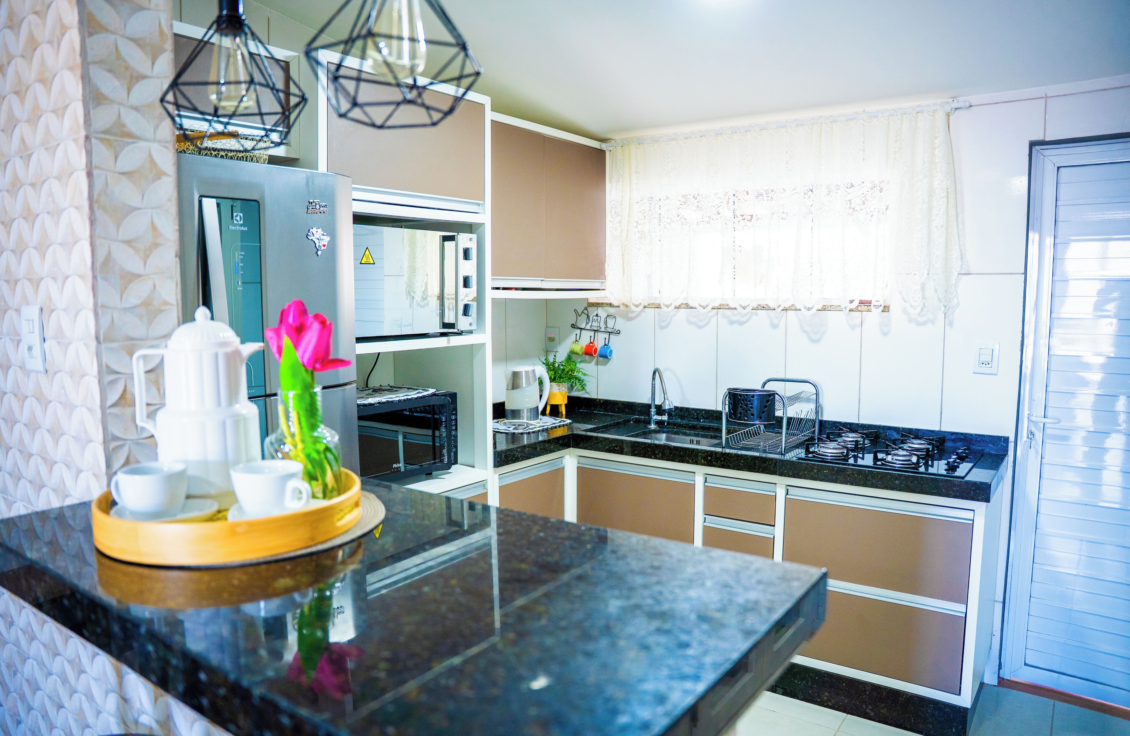 A modern kitchen with a black countertop, stainless steel appliances, and a window with lace curtains.